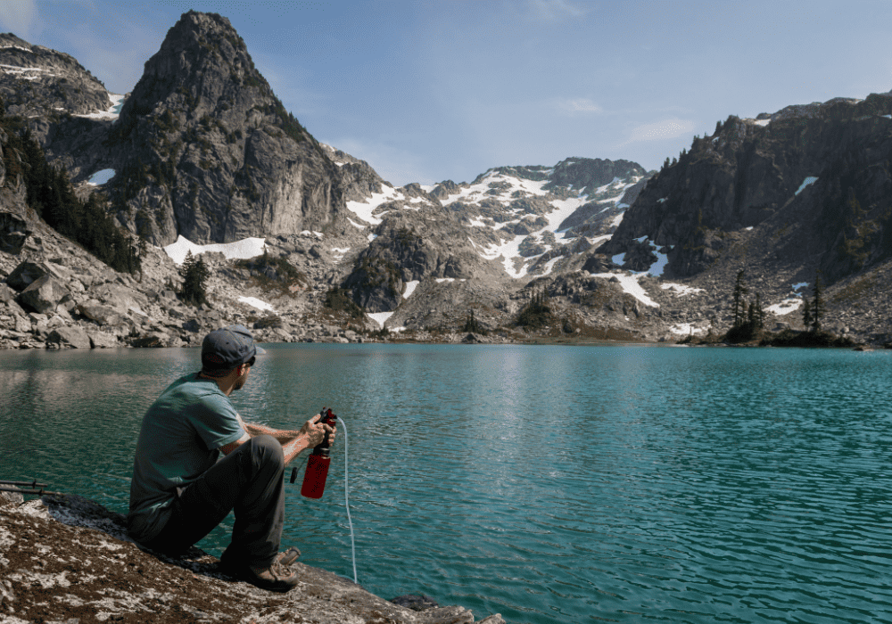 guy filling up a water bottle next to a lake